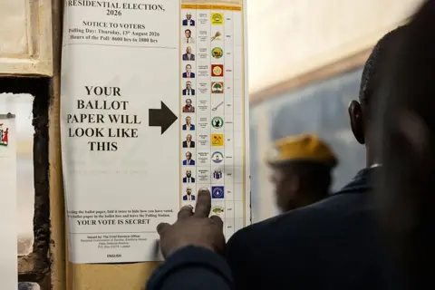AFP via Getty Images A specimen ballot paper is fixed to the wall. The back of a person's head can be seen as they look at the choice on offer.