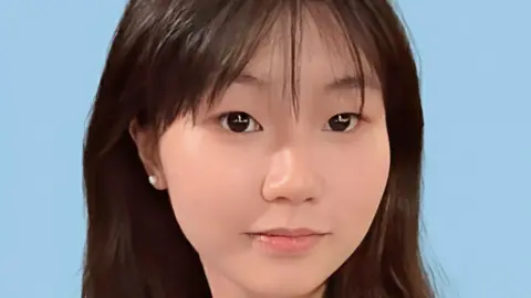 Aaple Wong Close-up of a young Chinese girl smiling at the camera, against a blue background