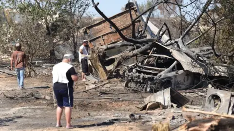EPA Jewish settlers, wearing religious garments, stand around the remains of a burnt building and car, in Havat Gilad (19/07/26)