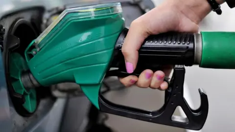 PA Media A close-up of a woman's hand, with pink nail varnish, holding a green petrol pump.