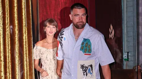 Jason Howard/Bauer-Griffin/GC Images Taylor Swift and Travis Kelce were seen walking out of a restaurant on their wedding weekend in New York City. She is wearing a floral dress and he is seen in a short-sleeved button-down shirt and pants. 