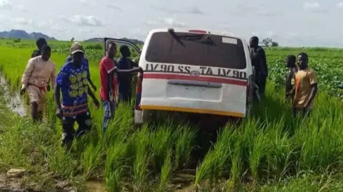 HQ Nigerian Army / Facebook A group of men in Nigeria gather around a white vehicle that is stuck in a muddy rural area surrounded by long grass