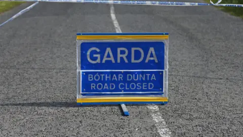 PA Media A blue sign placed on a road with white markings. The sign says Garda and road closed in both Irish and English. 