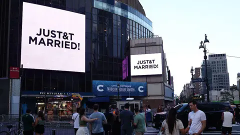 AFP via Getty Images People watch giant screens showing the message "JUST&T MARRIED!" (T&T for Taylor and Travis) outside Madison Square Garden, the reported venue for the wedding celebrations of pop singer Taylor Swift and pro-athlete Travis Kelce, in New York City on July 3, 2026.