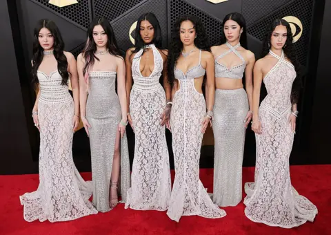 Getty Images Katseye members, from left to right, Yoonchae, Megan, Lara Raj, Manon, Sophia, and Daniela wear sparkling,floor-length gowns as they pose together on the red carpet for the 68th Grammy Awards in February 2026 in Los Angeles.
