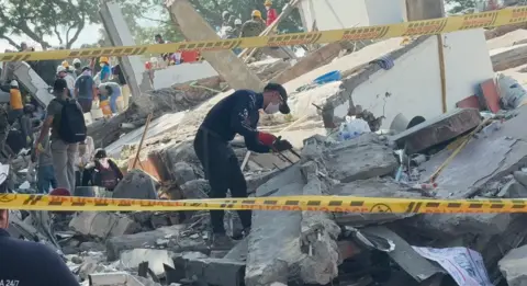 BBC News Mundo One man has a baseball bat and a facemask is using a handsaw to try and clear part of the rubble 

