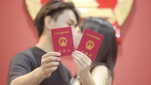 Getty Images A newly-wed couple pose for a photo with their marriage certificates in Yangzhou, Jiangsu Province of China.