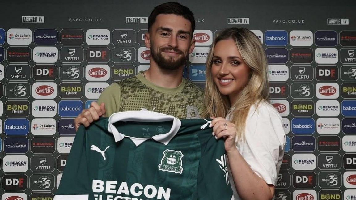 Owen and Jessica pose with a Plymouth Argyle shirt