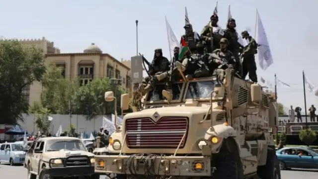 Afghan Taliban, celebrating the third anniversary of their takeover of Afghanistan, are piled into the bed of a military truck holding machine guns and flags outside the former US Embassy in Kabul
