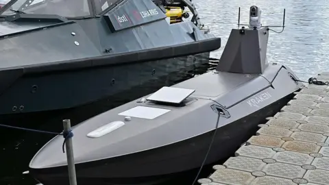 Getty Images A Kraken K3 Scout high-performance USV drone parked next to a larger boat with water shown behind it