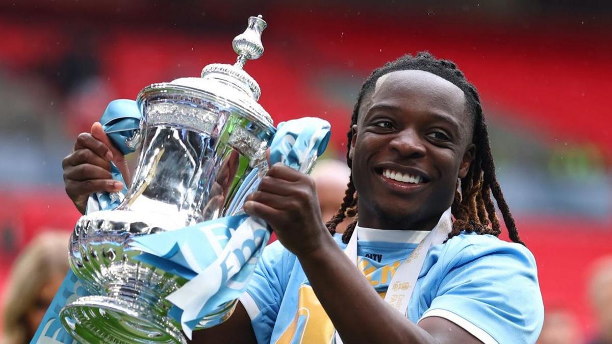 Manchester City Jeremy Doku smiles as he holds the FA Cup