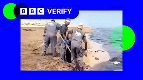BBC A screenshot from a video showing an oil slick in the water by a beach, with three men in overalls working to clean up the oil 