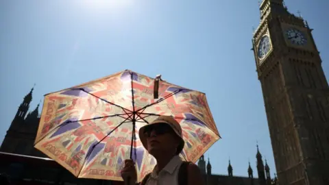 Reuters A woman covers from the sun with an umbrella during a heatwave in London, the UK. Photo: 13 August 2026