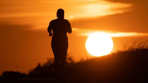 MATIAS BASUALDO/EPA/Shutterstock A woman jogs along a path as the sun rises in Frankfurt am Main, Germany, 09 July 2026. 