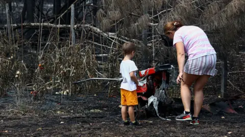 Reuters A woman and a toddler stand by charred ground and burned plants.