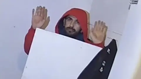 A man hiding in a cupboard with his hands in the air