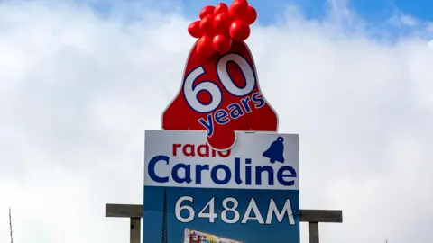 Getty Images Radio Caroline billboard celebrating the station's 60th birthday in 2024, it is blue and white with red balloons at the top.