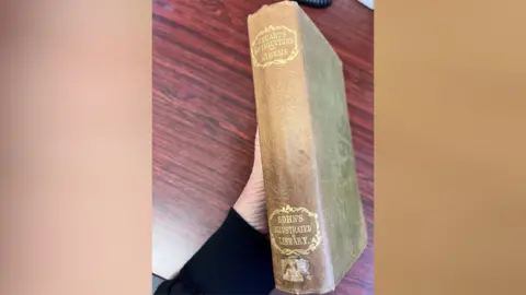 Kiama Council A partial hand holding an old book called Stuart's Antiquities of Athens with the spine showing
