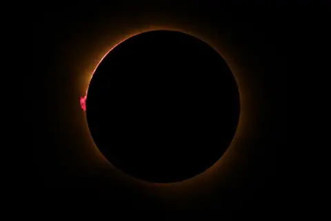 Cesar Manso/AFP/Getty Images A black darkened sky with a circle of orange light bordering a black circle – the blocked Sun - and small loops of pink can be seen coming from the surface of the Sun
