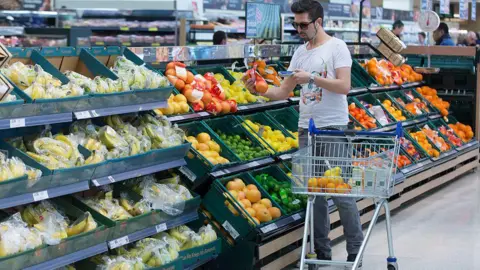Bloomberg via Getty Images A man wearing a t-shirt uses a hand-held device to scan a net of oranges as he shops in the fruit and vegetable aisle of a Tesco supermarket