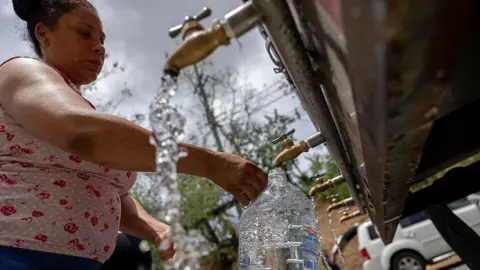 AFP via Getty Images A woman fills a large container of water at a public tap