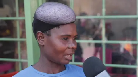 A head and shoulders image of Theresa Zulu wearing a blue T-shirt. She is turning to the right of the picture and is speaking into a microphone that is at the bottom right of the frame.