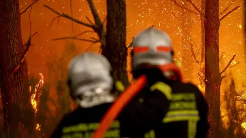 AFP via Getty Images Two firefighters direct a hose at a burning forest around 30km from Bordeaux, on July 26, 2026. 
