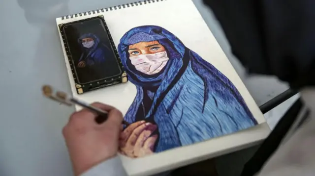 A girl's hand is shown drawing a picture of a veiled and masked woman with tears in her eyes.
