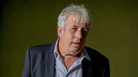 Corbis via Getty Images Rod Liddle looking up to his right, wearing a blue-striped shirt and navy jacket