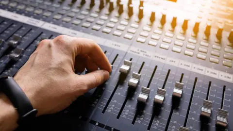 Getty Images A hand adjusting the knobs and faders on an audio mixer