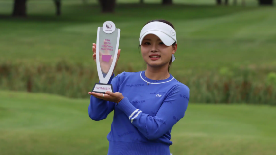 Jessica Bang posing for photographs on a golf course while holding a trophy