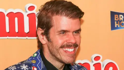 Paul Archuleta/Getty Images Perez Hilton smiles while attending an event in Hollywood in November 2022. He is wearing a vibrant blue suit with a bold pattern featuring snow flakes and characters from Super Mario. 