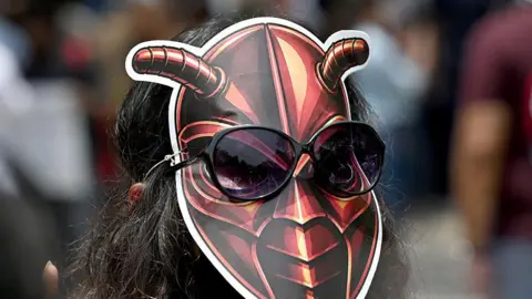 Hindustan Times via Getty Images A woman wearing a cockroach mask on the back of her head