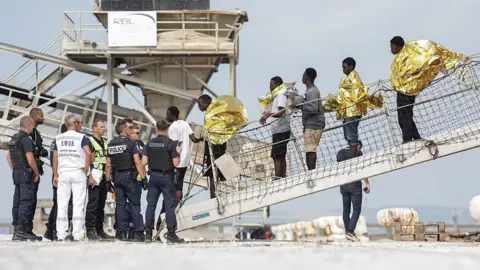 AFP via Getty Images Migrants disembark from the French rescue ship Minck following their rescue at sea