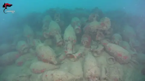 Carabinieri via AFP Dozens of barnacle-crusted jars seen on the sea bed