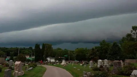 Getty Images  A person walks through Rose Hill Cemetery as a shelf cloud approaches behind them ahead of a severe thunderstorm. The clouds are grey and heavy in the sky. 