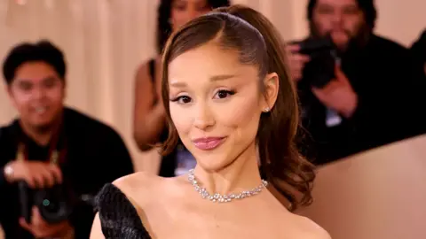Getty Images Ariana Grande poses for the cameras at the Golden Globes earlier this year. She is wearing a black dress and diamond necklace and has her hair in a ponytail.