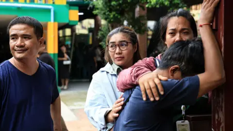 Getty Images  A person close to one of the victims reacts by leaning their head against a wall and people nearby to comfort him. 