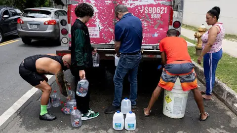 AFP via Getty Images A group of people filling up water containers at a truck