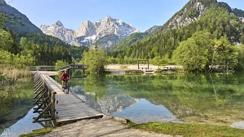 Getty Images Cyclist crossing a wooden boardwalk at Lake Jasna in Slovenia with the Julian Alps in the background (Credit: Getty Images)