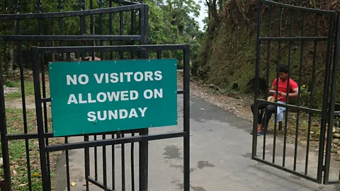 Jamie Fullerton A green sign reading "No visitors allowed on Sunday" hangs on an open gate at the entrance to Mawlynnong, India (Credit: Jamie Fullerton)