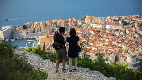 Ivan Vuković Two travellers stand at a rocky cliff overlooking the city of Dubrovnik (Credit: Ivan Vuković)