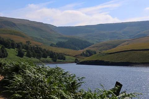 BBC/ Amy Wright The beginning of the walk winds around Kinder reservoir, nestled under Kinder Scout's steep ridge (Credit: BBC/ Amy Wright)